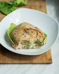 Sandwich with lettuce and ham on white plate. Wooden kitchen board on white table. Lettuce in the background.