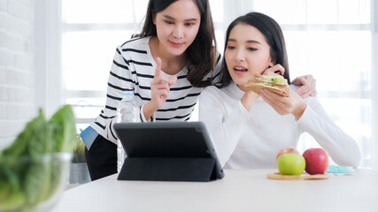 Happy Asian business friend having conversation in office.Two young business women sitting at table at home.  Teamwork, business meeting. Freelancers .eating breakfast sandwich.