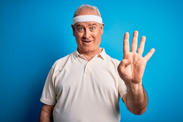 Naklejka premium Middle age hoary sportsman doing sport wearing sportswear over isolated blue background showing and pointing up with fingers number four while smiling confident and happy.