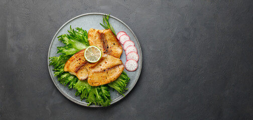 Grilled fish sea bass fillet with green lettuce and radish. Black stone background. Top view with copy space.