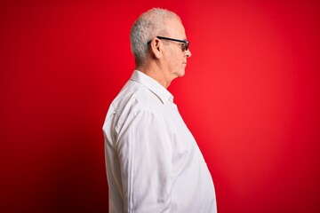 Middle age hoary man wearing funny sunglasses over isolated red background looking to side, relax profile pose with natural face with confident smile.