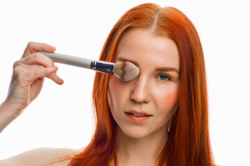 close beauty portrait of a red-haired girl with a brush for applying makeup. Isolated on a white background.