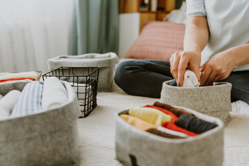 Woman folding clothes, organizing laundry in boxes and baskets. Concept of minimalist lifestyle and japanese t-shirt folding system. Minimalist wardrobe - obrazy, fototapety, plakaty