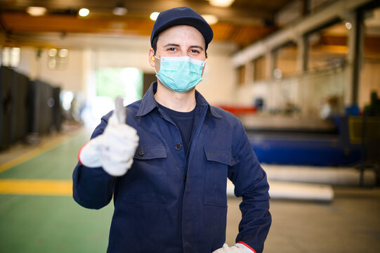 Portrait of a worker in an industrial plant wearing a mask and giving thumbs up, coronavirus concept