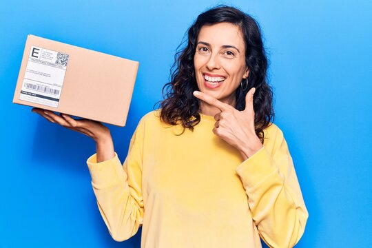 Young beautiful hispanic woman holding delivery package smiling happy pointing with hand and finger