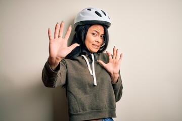 Young beautiful chinese woman wearing bike helmet over isolated white background afraid and terrified with fear expression stop gesture with hands, shouting in shock. Panic concept.
