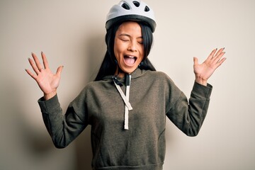 Young beautiful chinese woman wearing bike helmet over isolated white background celebrating mad and crazy for success with arms raised and closed eyes screaming excited. Winner concept