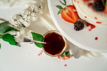 White berry cream cake decorated with strawberries and blackberries, among lilac flowers and green leaves. Food photography. Advertising and commercial close up design.