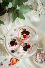 Meringue fruit cake garnished with cream and berries of cherries, blackberries and strawberries, among lilac flowers and green leaves. Food photography. Advertising and commercial close up design.