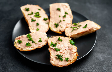 
Chicken pate on toast with fresh parsley on a black plate on a stone background