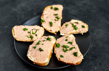 
Chicken pate on toast with fresh parsley on a black plate on a stone background