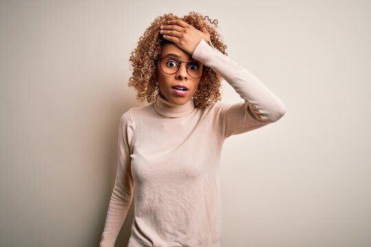 Young african american woman wearing turtleneck sweater and glasses over white background surprised with hand on head for mistake, remember error. Forgot, bad memory concept.