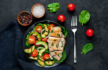 
Grilled chicken breast and grilled avocado salad with cherry tomatoes, spinach, in a black plate on a stone background