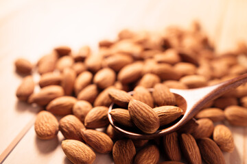 organic peeled brown almonds pour from wood spoon on wooden table. concept of vegan raw ingredient for vegetarian, snack and healthy food and high protein..