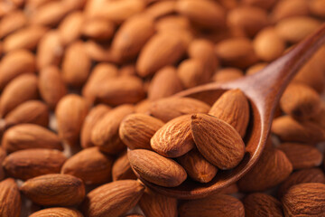 organic peeled brown almonds pour from wooden spoon. concept of vegan raw ingredient for vegetarian, snack and healthy food and high protein.