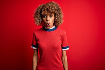 Young beautiful african american woman wearing casual t-shirt standing over red background afraid and shocked with surprise expression, fear and excited face.