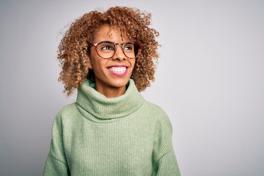 Young beautiful african american woman wearing turtleneck sweater and glasses looking away to side with smile on face, natural expression. Laughing confident.