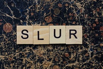 gray word slur from wooden letters in black font on a brown shabby wall with a pattern