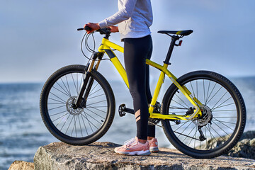 Fototapeta na wymiar Fitness sports woman cyclist with bicycle stands on the stones on the seashore. Athletic healthy people with active and sporty lifestyle