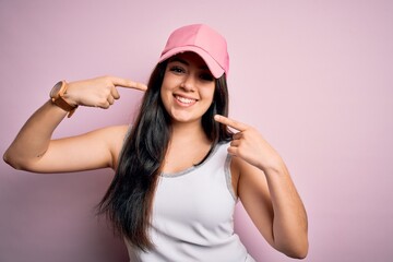Young brunette woman wearing casual sport cap over pink background smiling cheerful showing and pointing with fingers teeth and mouth. Dental health concept.
