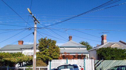 A row of detached houses in a St Kilda suburb. A telegraph pole has many crossing over cables...