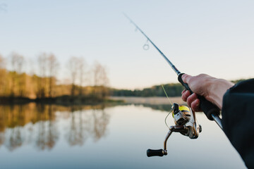 Fisherman with fishing rod in his hand catches fish on a boat. Fishing Day. Spinning in hand on pond background.