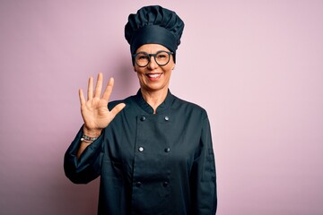 Middle age brunette chef woman wearing cooker uniform and hat over isolated pink background showing and pointing up with fingers number five while smiling confident and happy.