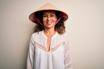 Middle age brunette woman wearing asian traditional conical hat over white background with a happy and cool smile on face. Lucky person.