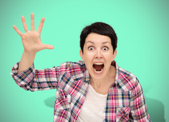 Angry woman isolated on neo mint background. Beautiful furious short haired brunette dressed casual plaid shirt shouting and waving her palm hand. Human emotions, facial expression concept.
