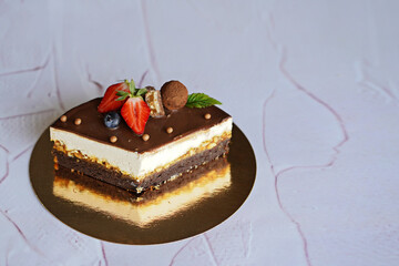 a quarter of a chocolate cake Snickers cut on a white background on a gold backing decorated with chocolate, sweets, fresh berries