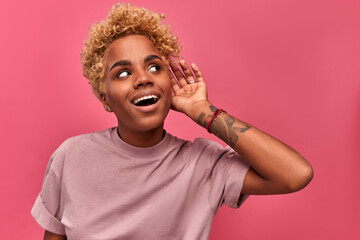 Funny young african american young girl smiling and eavesdrops looking to the right on a pink...