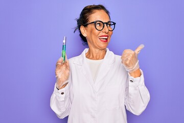 Middle age senior scientist woman wearing laboratory coat holding research test tube pointing and showing with thumb up to the side with happy face smiling