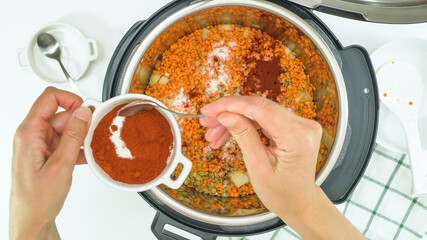 Multi cooker lentil soup recipe. Chef adds smoked paprika into pot, close up view from above