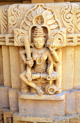 figure sculpture of a sitting woman in stone on a bas-relief wall of a temple, India