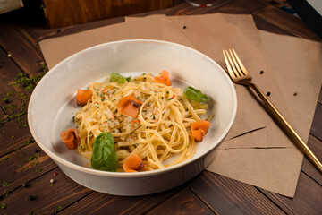 Plate of pasta with smoked salmon and herbs leaves on a wooden table.