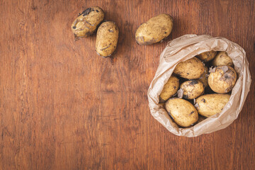 Raw new potatoes in a paper bag on wooden table. Fresh homegrown produce, Top view and large copy space for text
