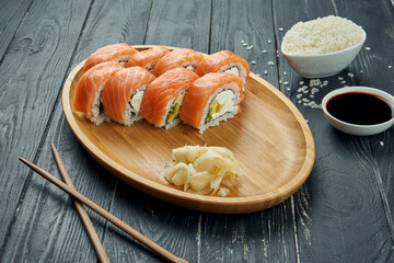 Classic japanese sushi rolls - philadelphia rolls with cream cheese, avocado and salmon on a bamboo plate on a black wooden background