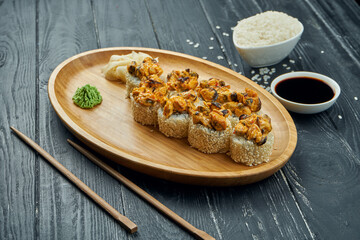 Classic japanese sushi rolls - baked rolls with cream cheese, spicy sauce and mussels on a bamboo plate on a black wooden background