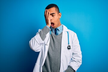 Handsome african american doctor man wearing coat and stethoscope over blue background Yawning tired covering half face, eye and mouth with hand. Face hurts in pain.