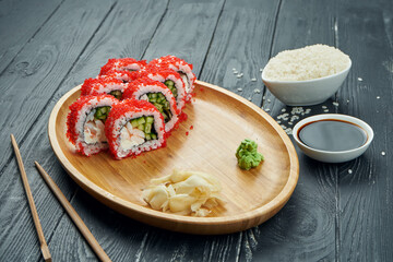 Classic japanese sushi rolls - california roll with tobiko caviar, cucumber and shrimp on a bamboo plate on a black wooden background