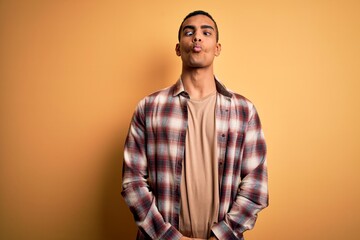 Young handsome african american man wearing casual shirt standing over yellow background making fish face with lips, crazy and comical gesture. Funny expression.