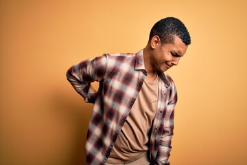 Young handsome african american man wearing casual shirt standing over yellow background Suffering of backache, touching back with hand, muscular pain