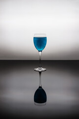 Glass of blue glitter drink on black glass. Sparkling blue wine.