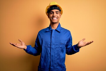 Young handsome african american worker man wearing blue uniform and security helmet smiling showing both hands open palms, presenting and advertising comparison and balance