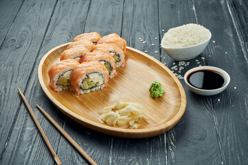 Classic japanese sushi rolls - philadelphia rolls with cream cheese, cucumber and salmon on a bamboo plate on a black wooden background