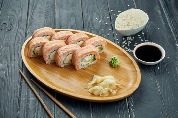 Classic japanese sushi rolls - philadelphia rolls with cream cheese, cucumber and grilled salmon on a bamboo plate on a black wooden background