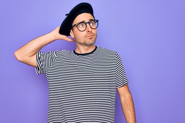 Handsome man with blue eyes wearing striped t-shirt and french beret over purple background confuse and wondering about question. Uncertain with doubt, thinking with hand on head. Pensive concept.