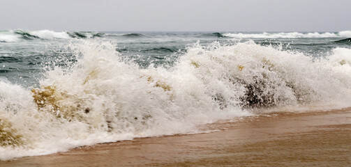 a wave with spray rolls on the sand and beach