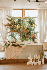 The table of the newlyweds, the presidium, with a gray linen tablecloth, a composition of flowers, on the background a lattice decorated with tropical leaves and branches of raspberries