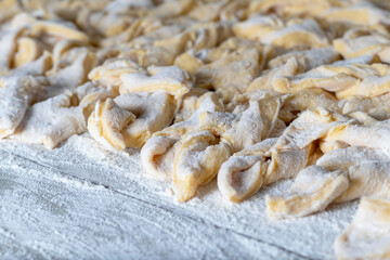 kitchen table. Sprinkled with flour. On it are dough products. Brushwood. Close-up